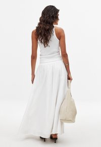 Jupe maxi blanche avec un design fluide, en tissu léger et taille élastique. Associée à un débardeur blanc ajusté et un sac beige.