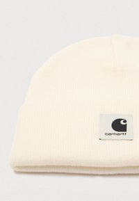 Off-white ribbed knit beanie with folded cuff and small square Carhartt logo patch sewn on the front right side.