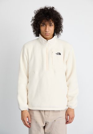 Fleece-pullover i off-white med halvdragkedja, bröstficka och svart logotyp på vänster sida. Mjuk textur och avslappnad passform.