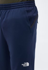 Κοντινό πλάνο σε σκούρο μπλε φόρμα The North Face με ελαστική μέση και φερμουάρ στην πλαϊνή τσέπη.