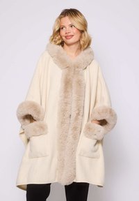 Poncho de color crema de gran tamaño con un suave borde de piel sintética beige en la capucha y las mangas. Cuenta con bolsillos y una silueta relajada.