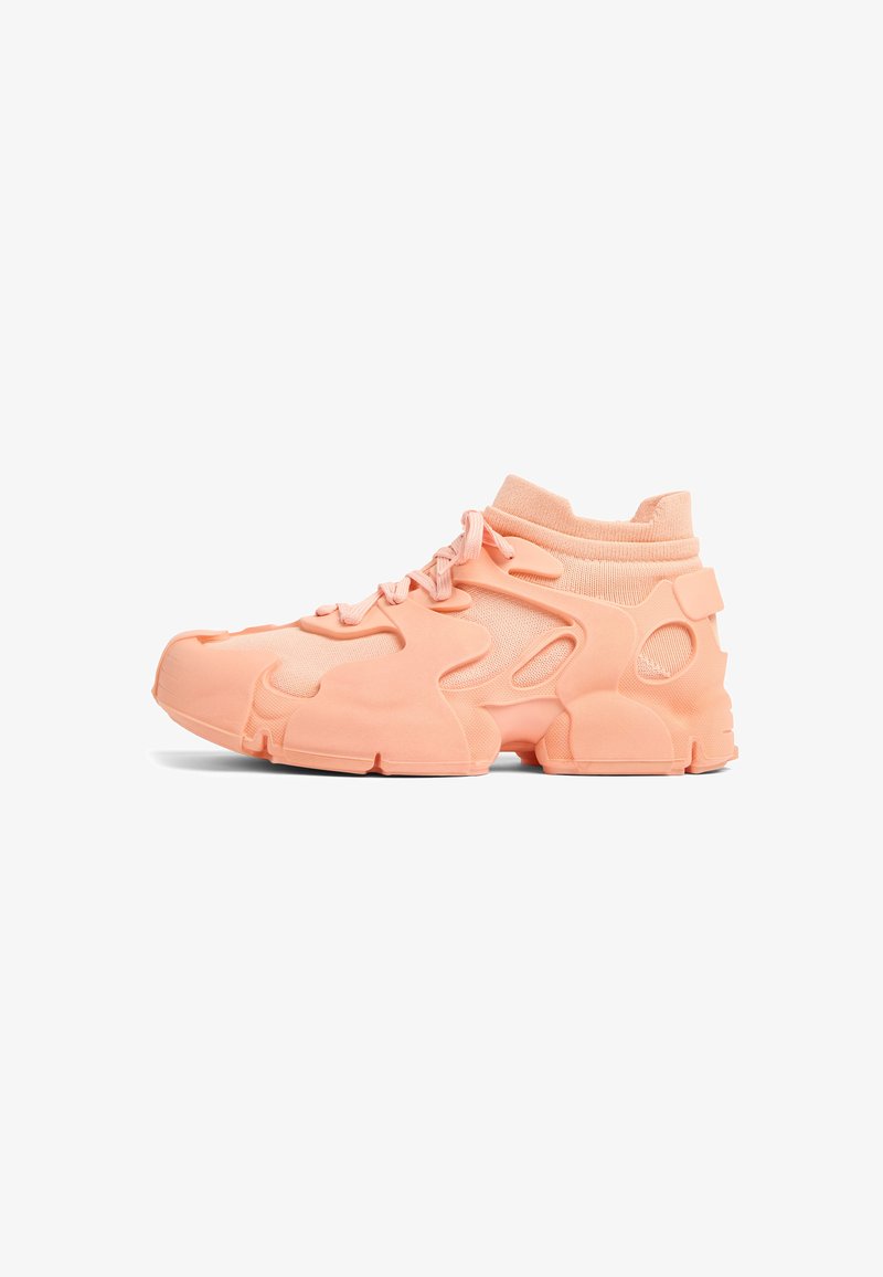 Athletic sneakers in soft peach color, featuring a textured rubber upper, mesh panels, padded collar, and chunky outsole with cutouts.