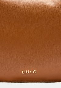 Borsa a tracolla in pelle marrone con una texture a granuli, dotata di un logo dorato nella parte inferiore e una chiusura con zip lungo il bordo.