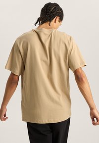 Beige bavlněn�é tričko s krátkým rukávem, volný střih a jednoduchý design. Má kulatý výstřih a prošívané detaily na lemu.