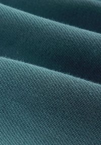 Hustý tmavozelený textil s hladkým povrchom a tesným tkaním, ktorý ukazuje jemné variácie a vlákna v celom materiáli.