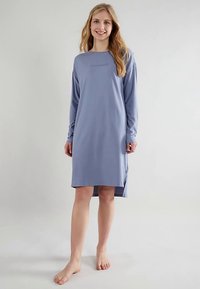 Nachthemd mit langen Ärmeln aus weichem, hellviolettem Stoff. Verfügt über einen runden Halsausschnitt und einen kleinen Logotext auf der Brust. Bis zur Mitte des Oberschenkels lang.