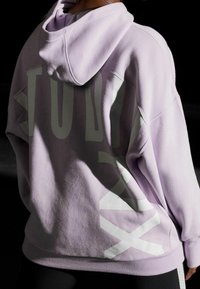 Sudadera de gran tamaño en color lavanda con una textura suave, que presenta diseños gráficos en blanco en la parte trasera. Incluye capucha y dobladillo inferior acanalado.