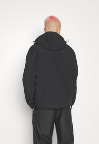 Svart vattentät jacka med huva, elastiska ärmslut och justerbar dragsko. Har quiltade detaljer och en avslappnad passform.