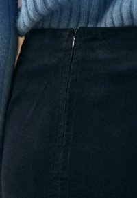 Jupe en velours côtelé bleu foncé avec un détail de fermeture éclair visible, présentant une texture lisse et un motif subtil de côtes verticales.