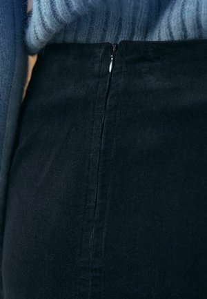 Tamsiai mėlynas korduro sijonas su matoma užtrauktuko detale, pasižymintis lygiu paviršiumi ir subtiliu vertikaliu juostelių raštu.