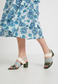 Flerfärgade klacksandaler med gröna, ljusblå och krämfärgade remmar, med blockklack och öppen tå-design.
