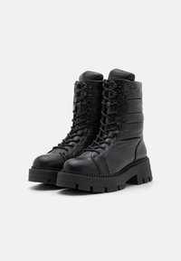 Botas de tobillo negras con cordones, con parte superior acolchada, que presentan una suela de goma gruesa y un acabado de piel suave. Diseño resistente con acentos laterales.