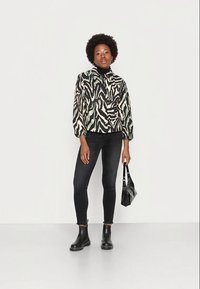 Jaqueta com estampado de zebra em preto e branco, jeans justos pretos, botins pretos e uma pequena bolsa preta. A jaqueta possui mangas bufantes.