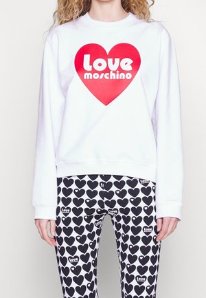 Biała bluza z dużym czerwonym sercem i tekstem "Love Moschino", w zestawie z białymi legginsami pokrytymi czarnymi sercami i małym tekstem "Love Moschino".