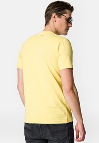 Żółta koszulka z krótkim rękawem wykonana z miękkiej bawełny. Posiada okrągły dekolt i małe logo z tyłu, zestawiona z ciemnymi dżinsami.