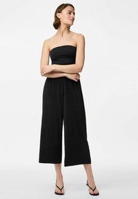 Svart strapless jumpsuit i texturerad tyg, med vida ben och avslappnad passform. Det är matchat med svarta sandaler med remmar.