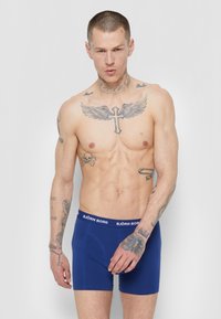 Sötétkék boxer alsónadrág rugalmas anyagból, kontrasztos fehér "BJÖRN BORG" derékpánttal és varrott részletekkel.