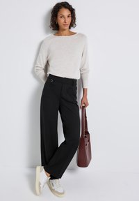 Pull crème à manches longues, pantalon noir à jambes larges avec deux poches avant, et sac à main bordeaux, complété par des baskets blanches et grises.