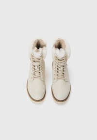 Bottines beige clair avec doublure en fourrure, design à laçage et semelle texturée. Présente des accents en matériel doré et une surface douce et lisse.