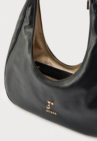 Czarna skórzana torebka o gładkiej fakturze, z elementami w kolorze złotym i zamknięciem na suwak. Wnętrze ozdobione jest wzorem z logo oraz posiada kieszeń na zamek.