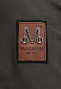 Leather label in brown with embossed "M" and silver hardware rivets on a textured black background, featuring "MARIKOO EST 2016" text.