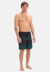 Herre svømmebukser med et sort og teal stribet mønster, lavet af letvægtsmateriale, med elastisk talje og snor.