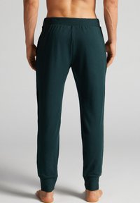 Donkergroene jogger broek gemaakt van zacht, rekbaar materiaal. Voorzien van een elastische tailleband en taps toelopende boorden met zijzakken. Soepele textuur.