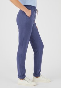 Marineblaue Sweatpants aus weichem Material, mit einem Kordelzugbund, seitlichen Taschen und umgeschlagenen Säumen, kombiniert mit weißen Sneakers.