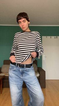 Fekete-fehér csíkos hosszú ujjú felső fekete mandzsettával, világoskék, bő szabású farmernadrággal és fekete övvel párosítva.