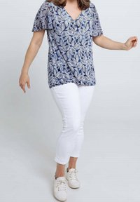 Marineblauw, kortärmeliges Oberteil mit weißem Blattmuster, V-Ausschnitt; kombiniert mit weißen, eng anliegenden Hosen und weißen Turnschuhen.