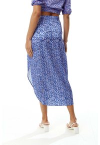 Blue maxi skirt with a flowing design, featuring a patterned texture of white and light blue shapes. Side slit visible, paired with white shoes.