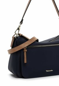 Marineblaue Lederhandtasche mit glatter Textur, braunem Schulterriemen, silberner Hardware und einer Reißverschlusstasche auf der Vorderseite. Markenlogo angezeigt.