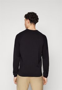 Schwarzer Strickpullover mit gerippten Akzenten an den Schultern. Hat lange Ärmel und einen runden Ausschnitt, von der Rückansicht dargestellt.
