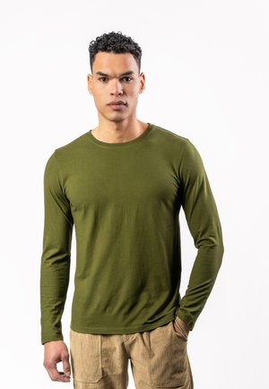 Olivgrünes Langarm-T-Shirt aus weicher Baumwolle, mit rundem Halsausschnitt und enganliegenden Ärmeln, kombiniert mit beigen strukturierten Hosen.