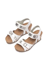 Sandales blanches avec des lanières et une boucle en argent métallique, design ouvert à l'avant, semelle en liège compensée et texture de chaussant en daim marron.
