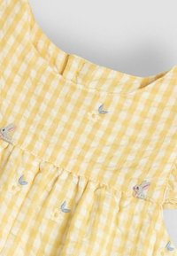 Vestido de cuadros amarillos con mangas cortas, con bordados de flores y conejos. Tejido ligero con frunces en la cintura.