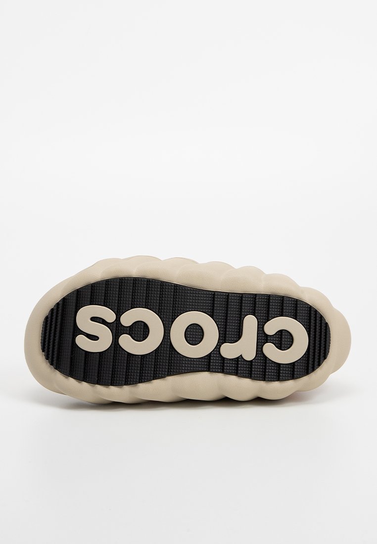 Helle beige Crocs-Sohle mit gepolstertem Rand, strukturiertem schwarzen Gummi-Oberfläche und erhobenem "CROCS"-Logo in Creme.
