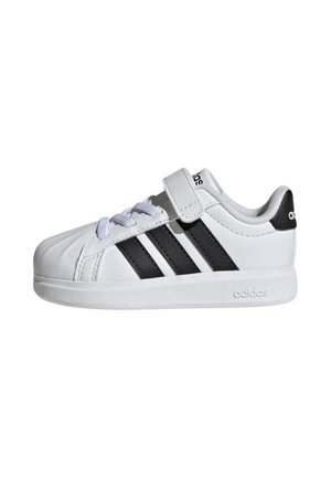 Sneaker bianca Adidas con strisce nere, lacci e una fascia in velcro, vista di lato su sfondo bianco.