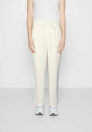 Ανοιχτόχρωμες κολάν παντελόνες με ελαστική μέση και κορδόνι, με χαλαρή εφαρμογή και ίσια πόδια, συνδυασμένες με γκρι αθλητικά παπούτσια.