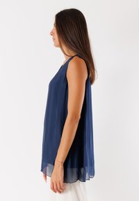 Top senza maniche di colore blu navy con un design ampio e fluido, caratterizzato da un collo a giro e un tessuto morbido e leggero con una leggera trasparenza.