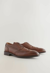 Chaussures en cuir brun avec détails de brogue, bout arrondi et accents texturés. Présentent une finition lisse et un talon bas.