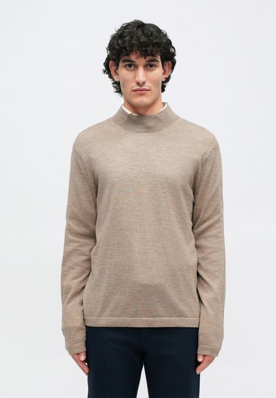 Bēšs vieglais džemperis ar augstu apkakli, garām piedurknēm un gludu tekstūru. Vienkāršs dizains, valkāts ar tumšiem biksēm.