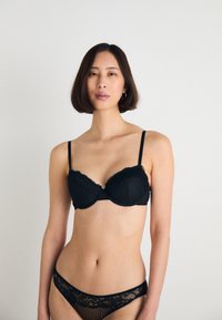 Sutiã preto com rendas, apresentando copas almofadadas com costuras verticais, combinado com uma tanga correspondente com intrincados padrões de renda.