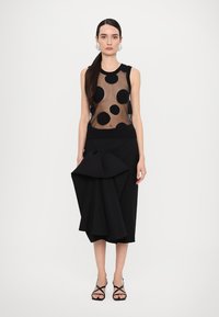 Black sleeveless top with sheer fabric and large black polka dots. Black skirt with a structured, draped detail at the front. Black strappy shoes.