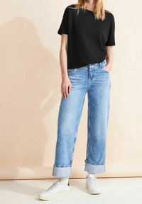 Černé pletené tričko spárované se světle modrými kalhotami s širokými nohavicemi; kalhoty mají ohrnuté lemy, no šeny s bílými teniskami. Jednoduchý, ležérní outfit.