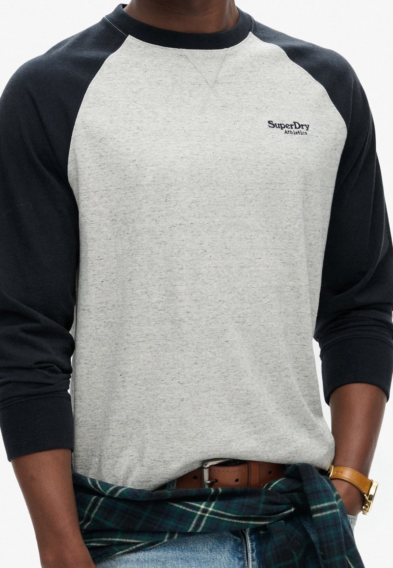 Grau und dunkelblaues Raglan-Langarmshirt mit gerippten Manschetten; verfügt über ein gesticktes "SuperDry Athletics"-Logo auf der Brust.