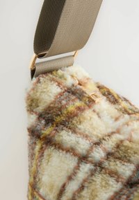 Torba na ramię z miękkiego, teksturowanego materiału w kratę w odcieniach beżu, brązu i żółci, z regulowanym brązowym paskiem i złotymi elementami.