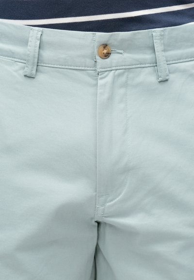 Βαμβακερές chinos ανοιχτό πράσινο χρώμα με κούμπωμα κουμπιού, διαθέτουν ομαλή υφή και πλευρικές τσέπες. Διακριτικές λεπτομέρειες ραφής είναι ορατές.