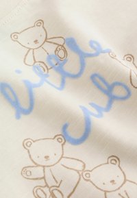 Tissu doux avec des illustrations d'oursons marron clair et un texte en cursive bleue texturée indiquant « petit ourson ».