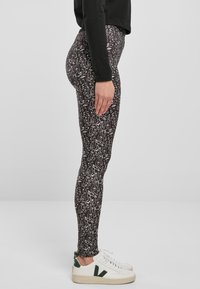 Leggings neri con un motivo astratto bianco, design a vita alta e materiale elastico. Abbinati a sneakers bianchi, in vista laterale.